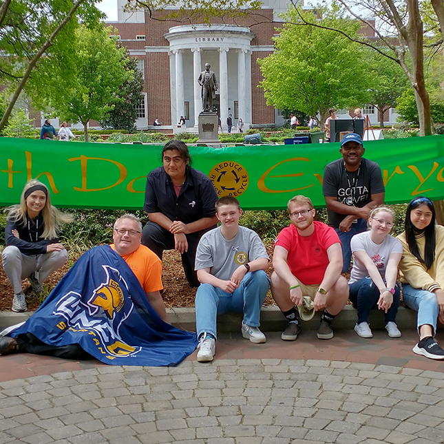 Students sitting on College Ave. in front of Jackson Library with a banner.